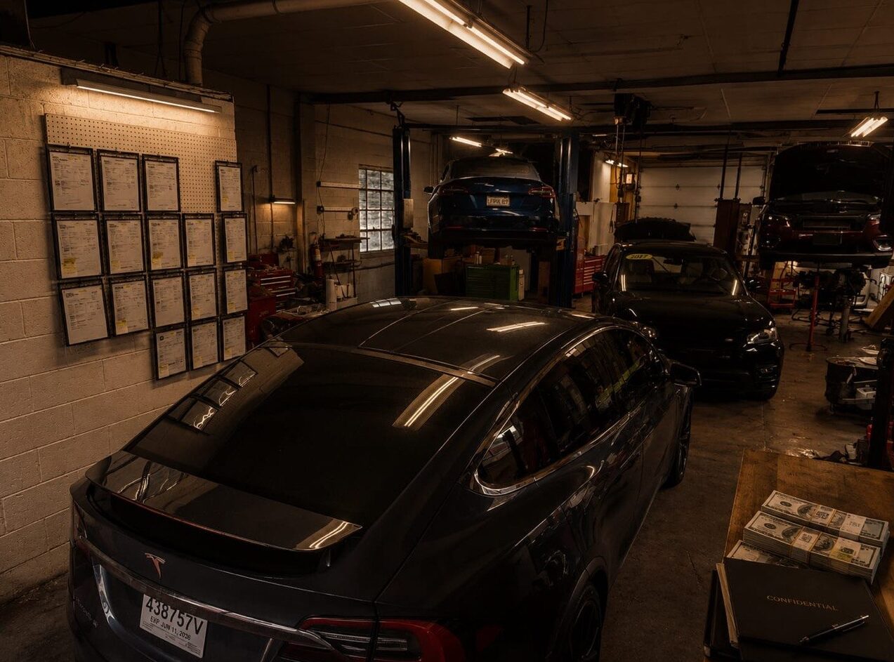 Inside the Iron Wolf Motors service bay in Worcester, MA — a Tesla on the lift alongside the alignment-certificate wall
